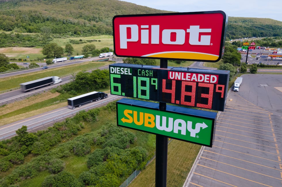 FILE - Trucks and cars drive by a Pilot Travel Center sign displaying fuel prices in Bath, New...